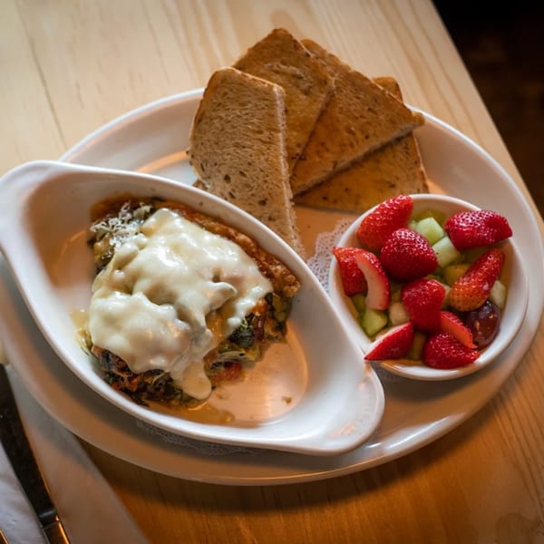 A baked dish with melted cheese, toast, and a side of fresh fruit on a white plate.