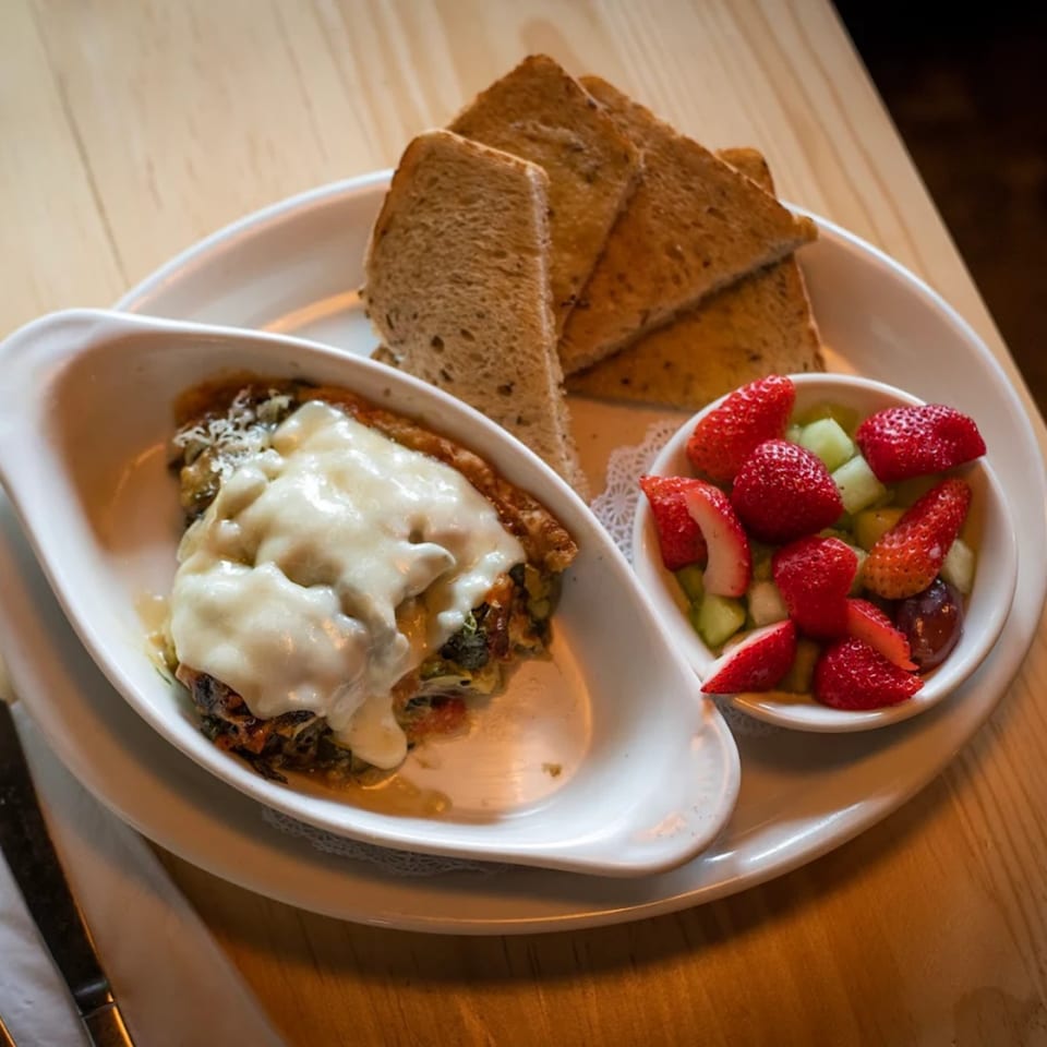 A baked dish with melted cheese, toast, and a side of fresh fruit on a white plate.