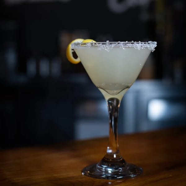 A martini glass with a light-colored drink, sugar-rimmed, and garnished with a lemon twist.