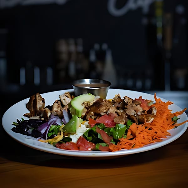 A vibrant Driftwood Cafe salad with grilled chicken, avocado, tomatoes, and shredded carrots.
