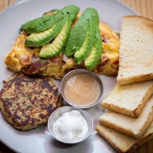 Driftwood Cafe's American breakfast with an omelet topped with avocado, a potato pancake, toast, applesauce, and sour cream.