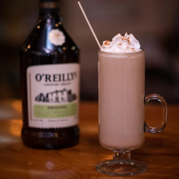 A tall glass of creamy Irish coffee with whipped cream and cinnamon next to a bottle of O'Reilly's.
