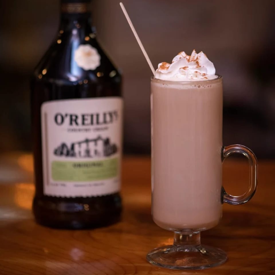 A tall glass of creamy Irish coffee with whipped cream and cinnamon next to a bottle of O'Reilly's.